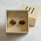 Pair of handcrafted sterling silver stud earrings with oval moss agate and carnelian gemstones, displayed in a cream Journey Through Jewellery gift box. Each one-of-a-kind gemstone features unique amber, green and black landscape-like inclusions, finished with mirror-polished bezels and handcrafted silver grain details.