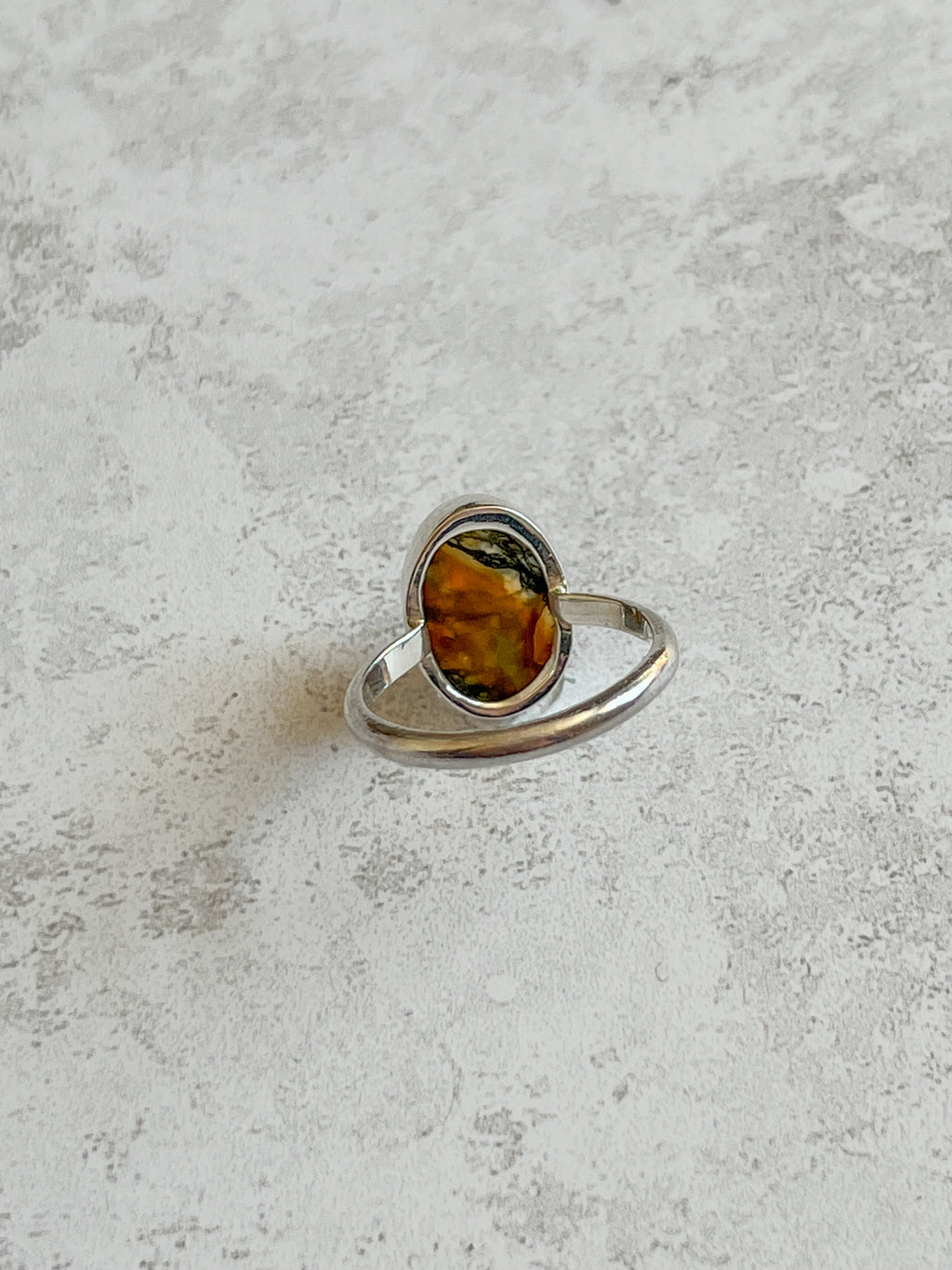 Handmade sterling silver ring with oval moss agate and carnelian gemstone, bezel set with an organically cut window on the back to let light through, set on a D-shaped band, photographed on a light textured background