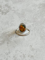 Handmade sterling silver ring with oval moss agate and carnelian gemstone, bezel set with an organically cut window on the back to let light through, set on a D-shaped band, photographed on a light textured background