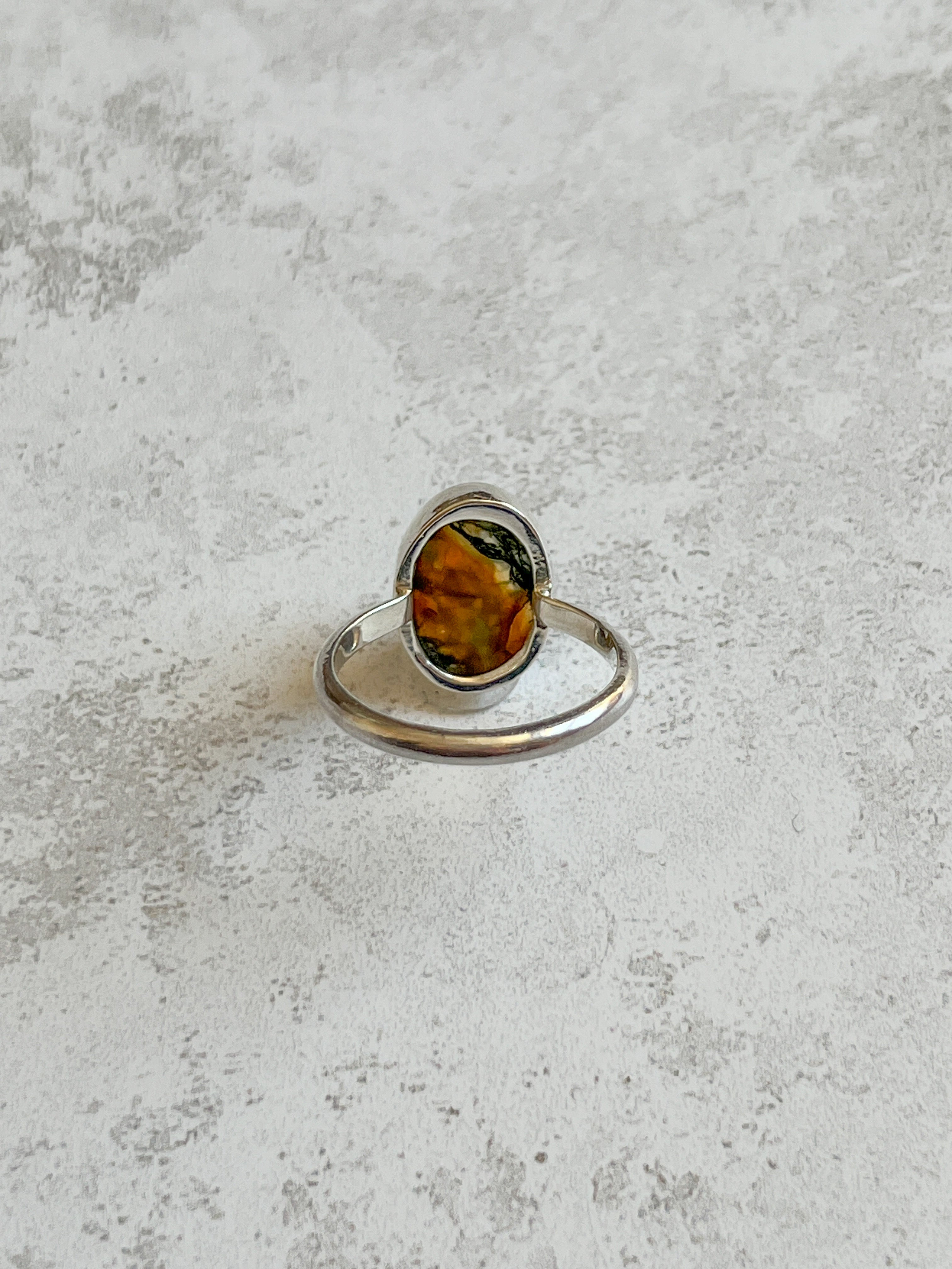 Handmade sterling silver ring with oval moss agate and carnelian gemstone, bezel set with an organically cut window on the back to let light through, set on a D-shaped band, photographed on a light textured background