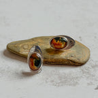 One-of-a-kind handcrafted sterling silver stud earrings featuring matching oval moss agate and carnelian gemstones with warm amber, deep green and natural landscape-like inclusions. Mirror-polished artisan earrings displayed on natural stone, with subtle variations making each gemstone unique