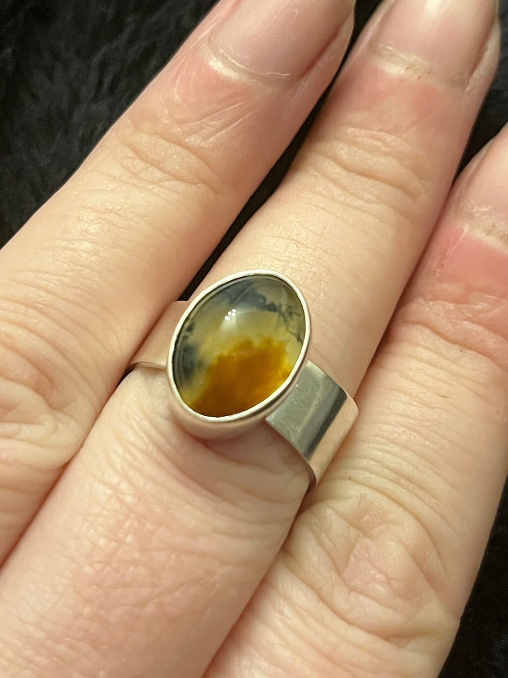 Hand wearing a ring with a colorful stone on a dark background
