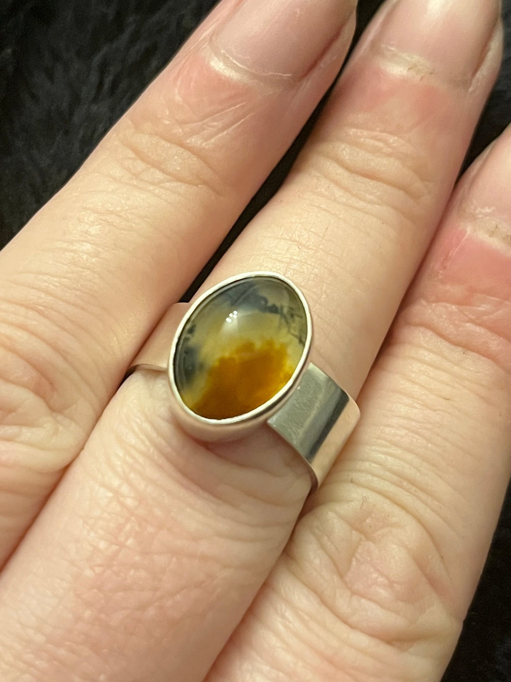 Hand wearing a ring with a colorful stone on a dark background