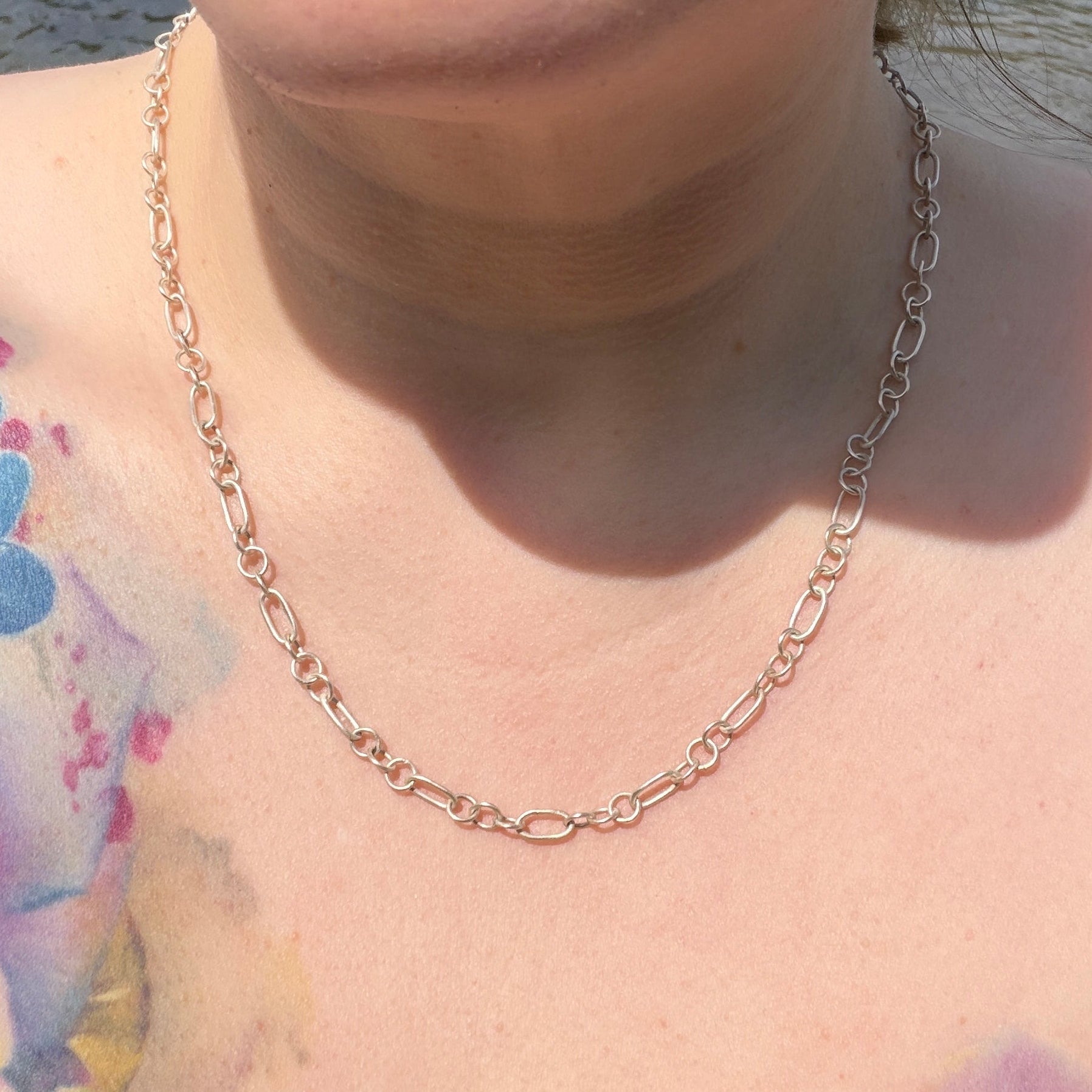 Close-up of a person wearing a silver chain necklace with tattoos visible on the shoulder.