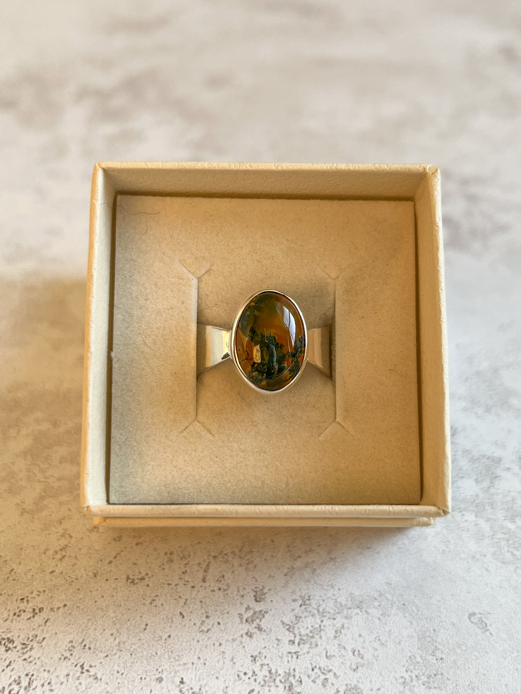 Handmade sterling silver ring with oval moss agate and carnelian gemstone in a bezel setting, artisan silver jewellery displayed in a neutral jewellery box, ready to ship.