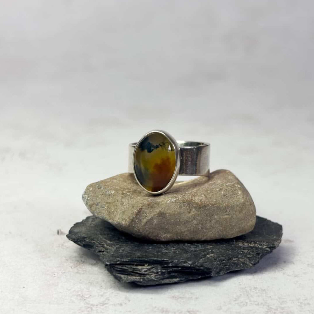 Silver ring with a colorful stone on a rock against a white background